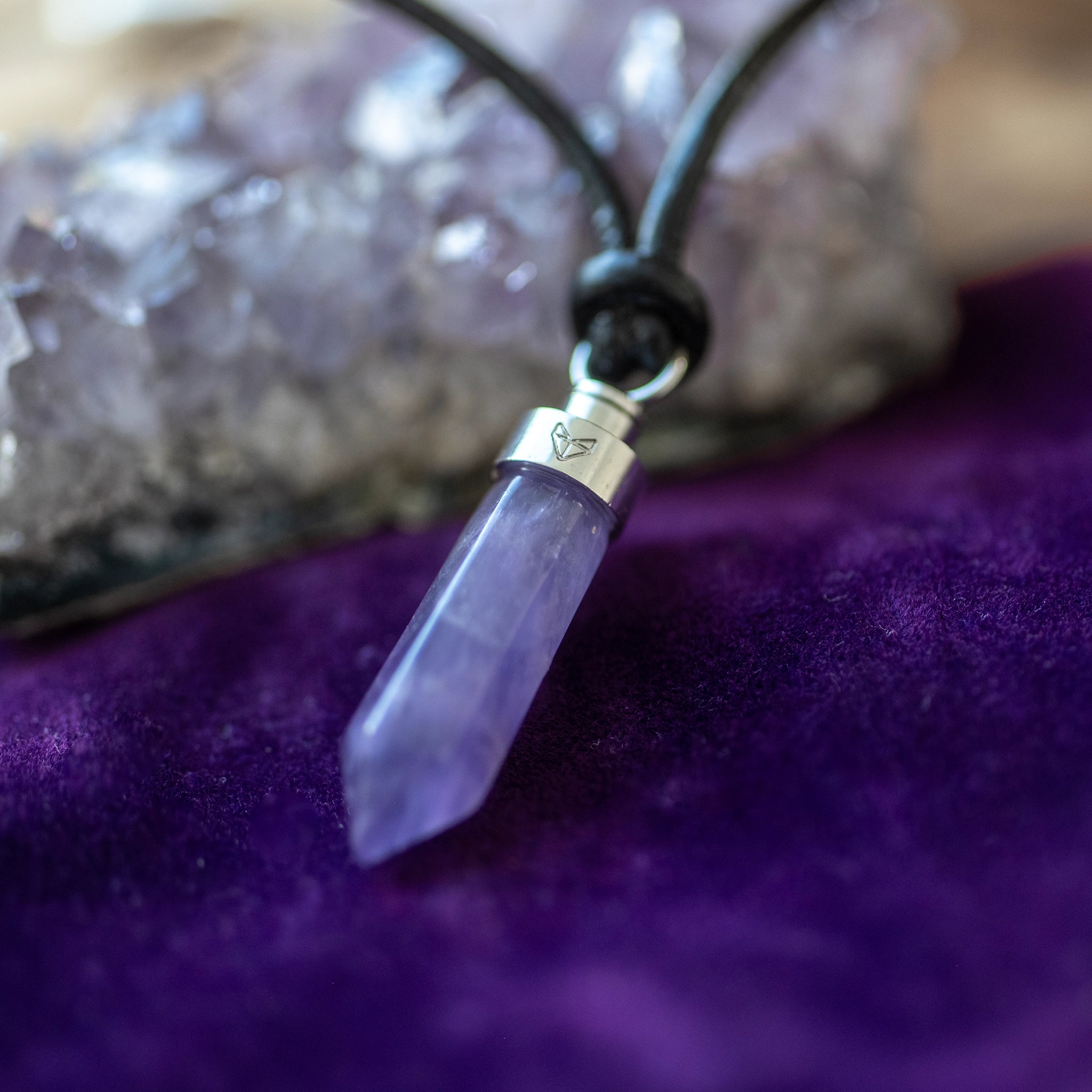 Amethyst crystal pendant on purple velvet beside raw amethyst geode