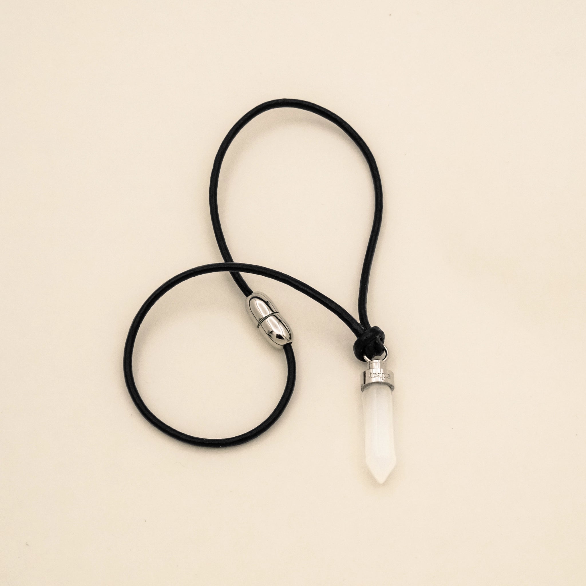 Clear quartz clarity pendant for cats on black leather cord with magnetic clasp on a beige background