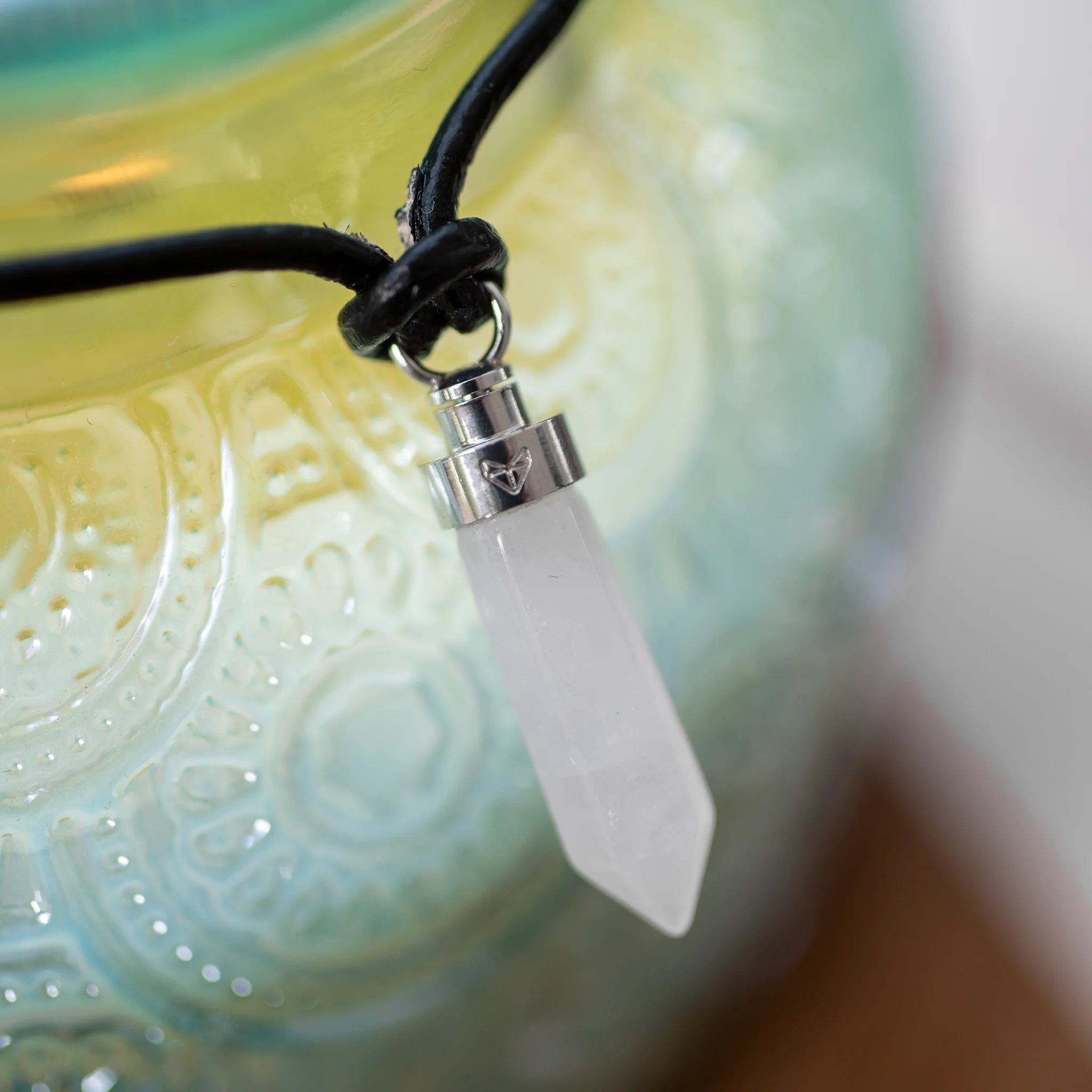 Close-up of clear quartz clarity pendant draped on a green ceramic bowl