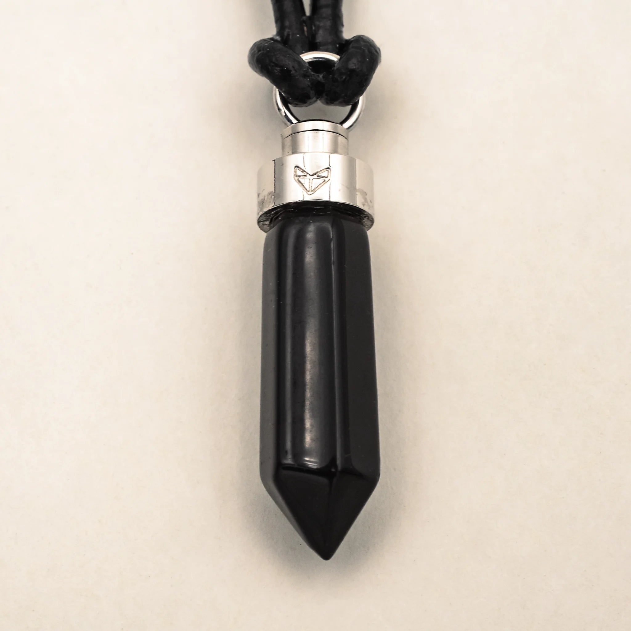 Close-up of obsidian protection pendant on black leather cord on a beige background