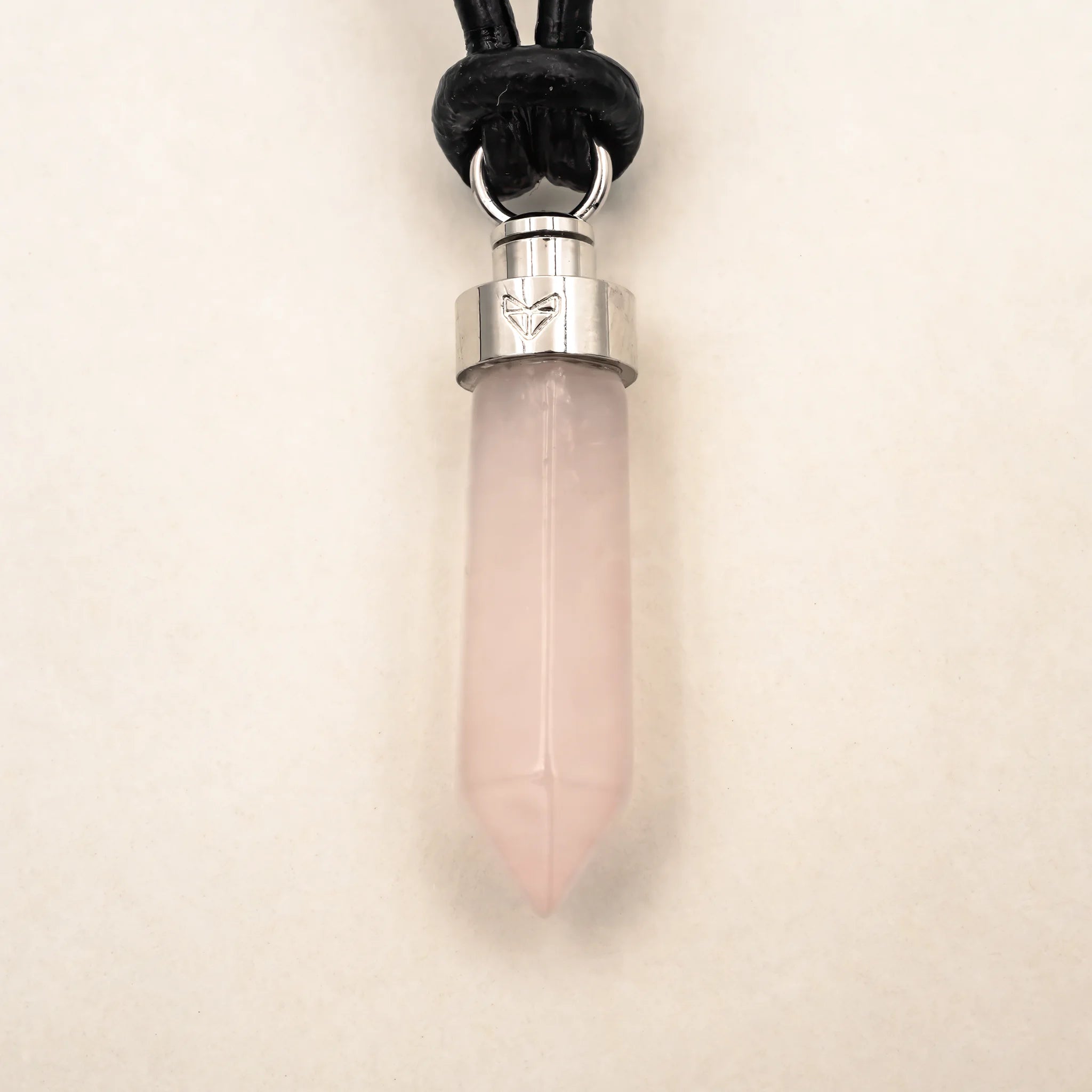 Close-up of rose quartz love pendant on black leather cord on a beige background