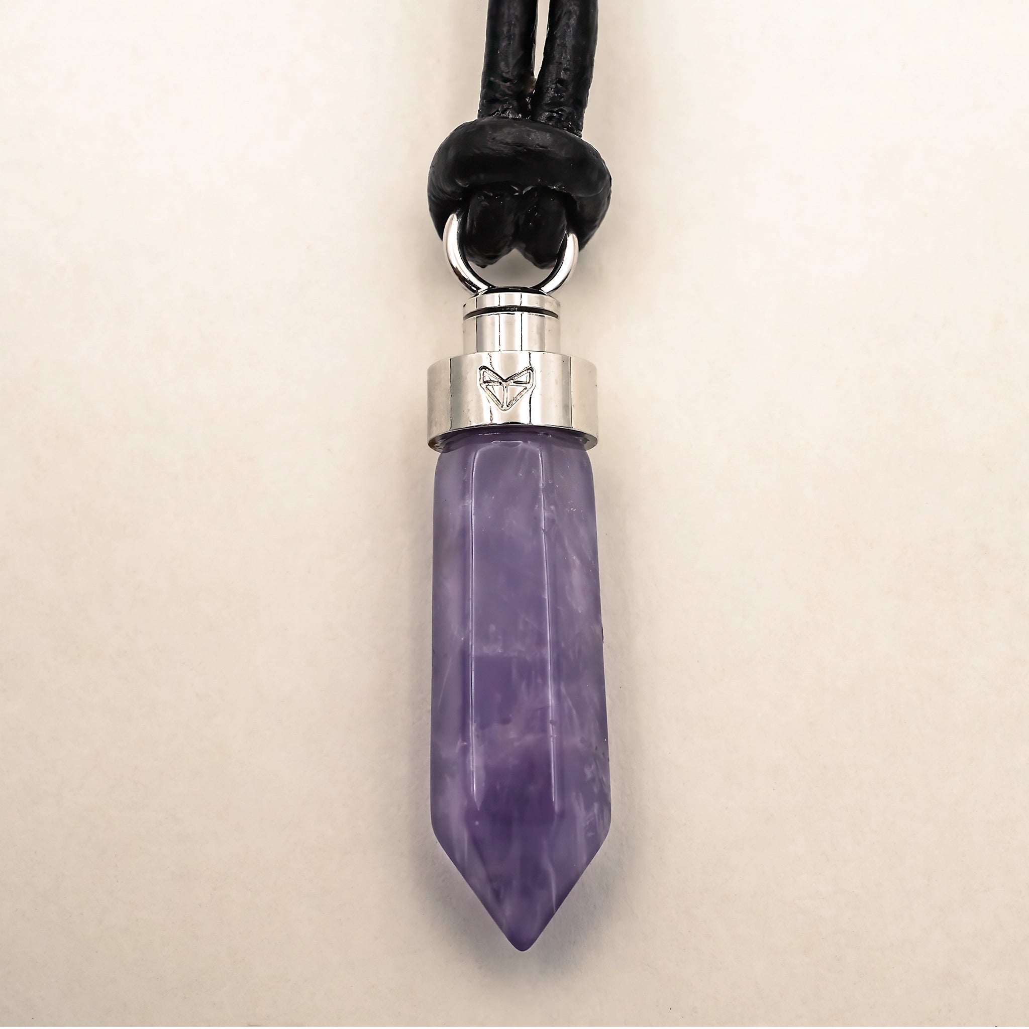 Close-up of amethyst calm pendant on black leather cord on a beige background