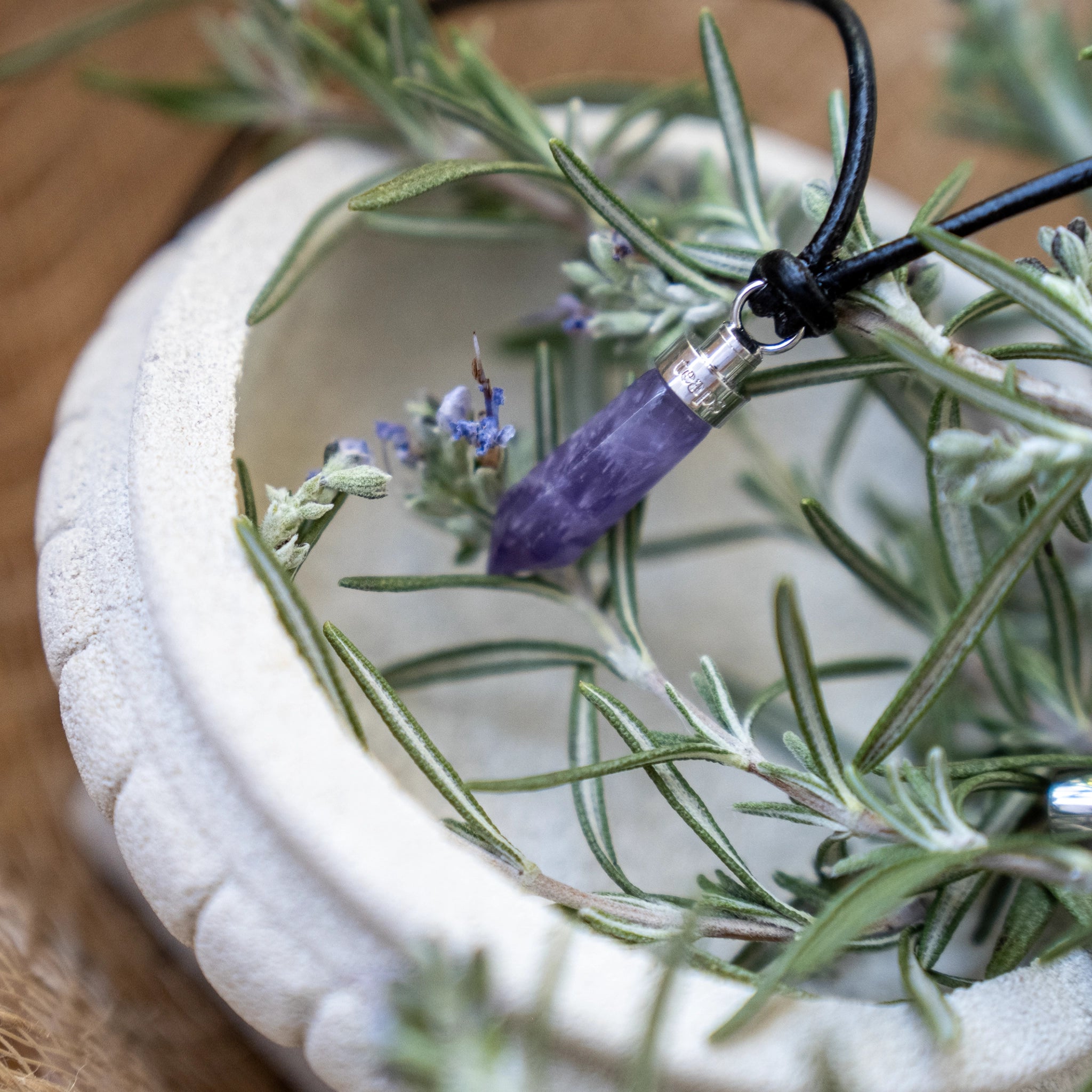 Amethyst calm pendant draped in white planter with fresh rosemary