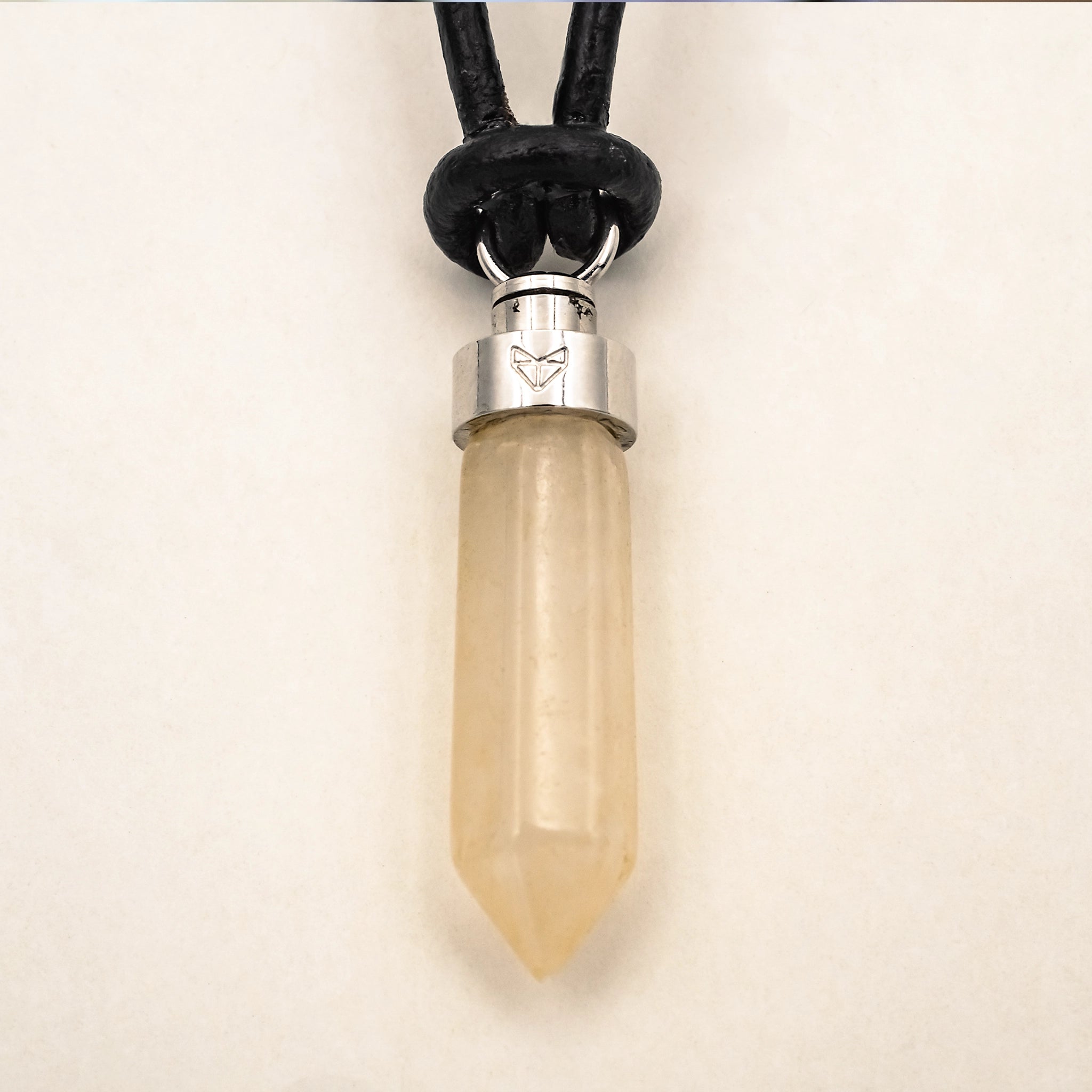 Close-up of citrine joy pendant on black leather cord on a beige background