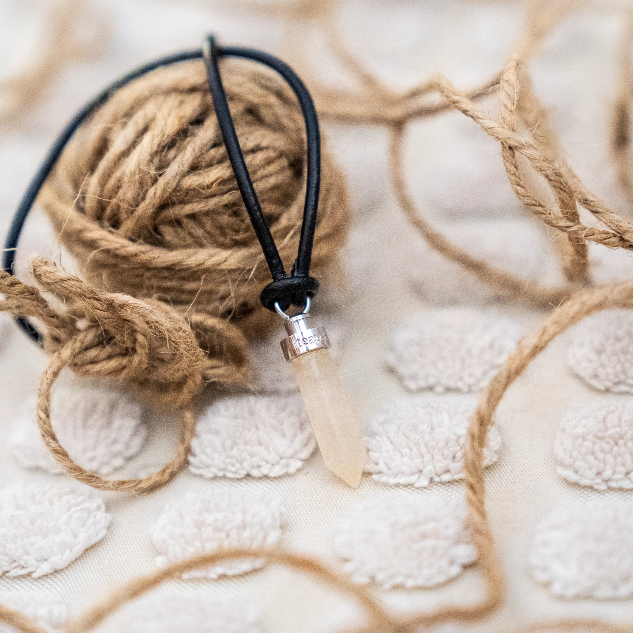 Citrine joy pendant resting on ball of twine on an off-white textured carpet