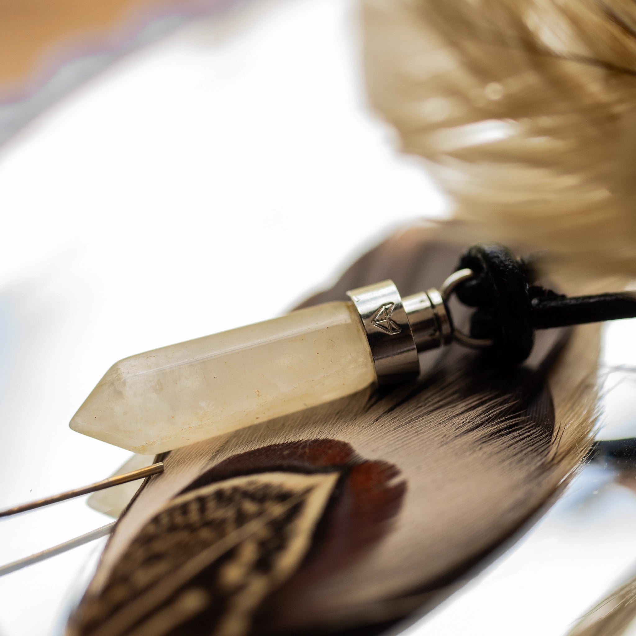 Close-up of citrine joy pendant beside a feather on a mirrored surface