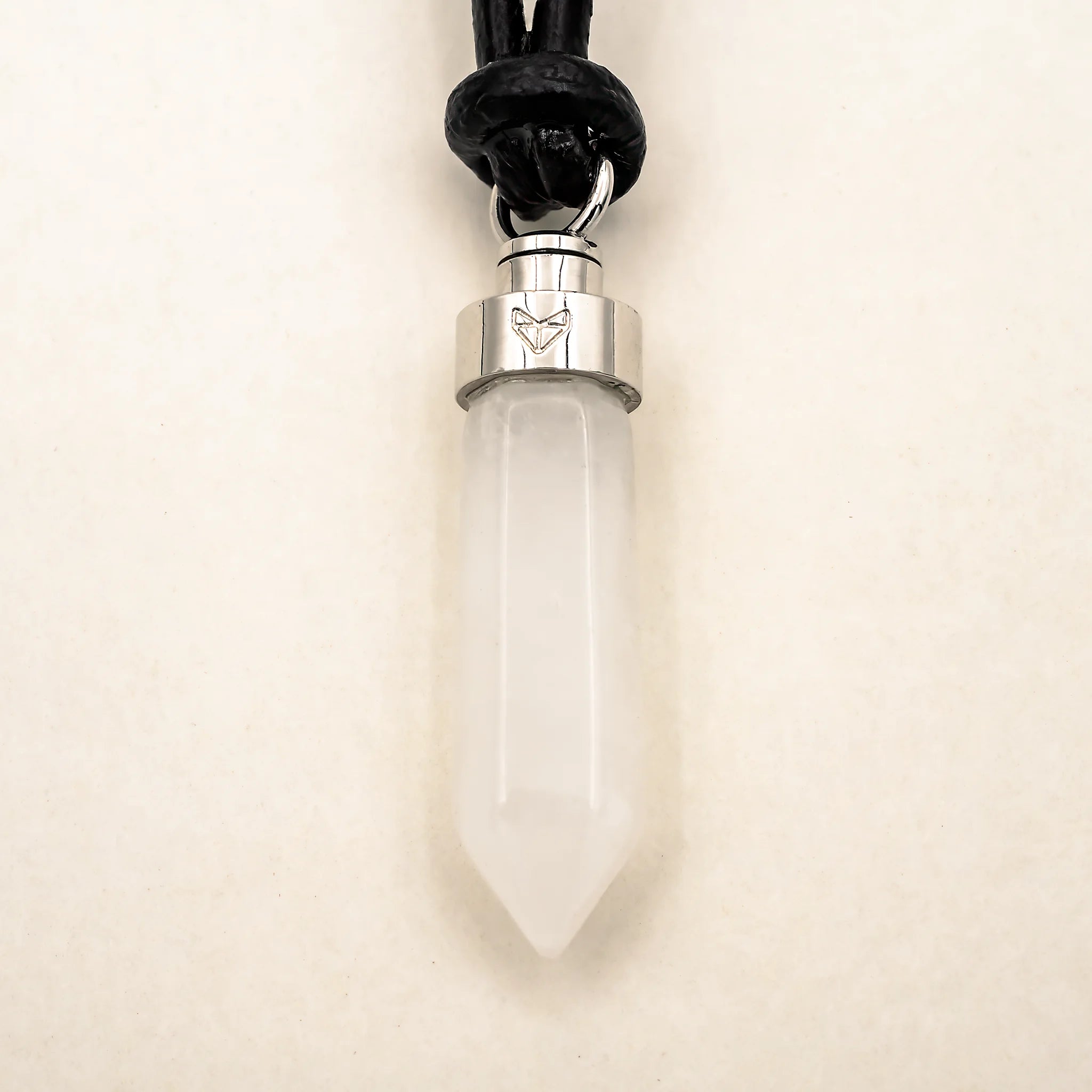Close-up of clear quartz clarity pendant on black leather cord on a beige background