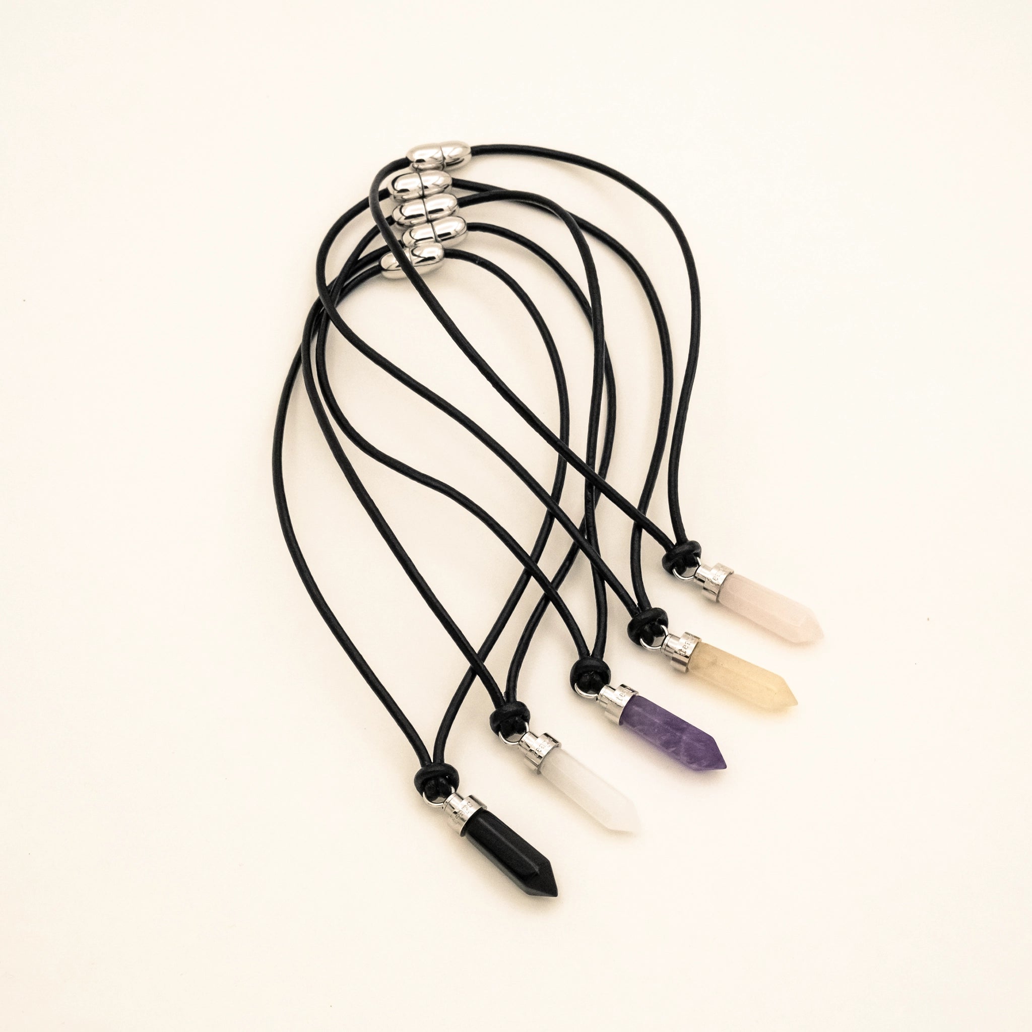 Complete ritual set of five crystal wellness pendants for cats on black leather cords on a beige background