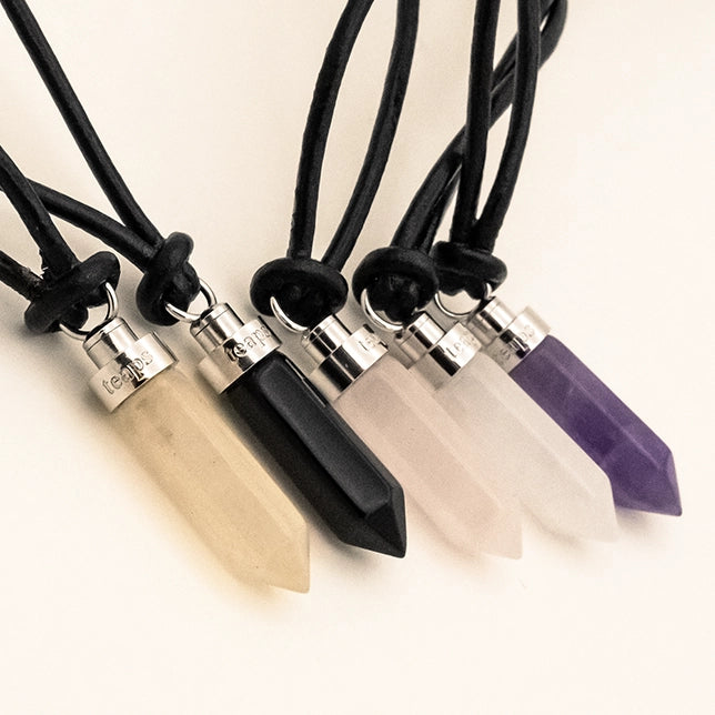 Five crystal cat pendants laid together showing citrine, obsidian, rose quartz, clear quartz, and amethyst