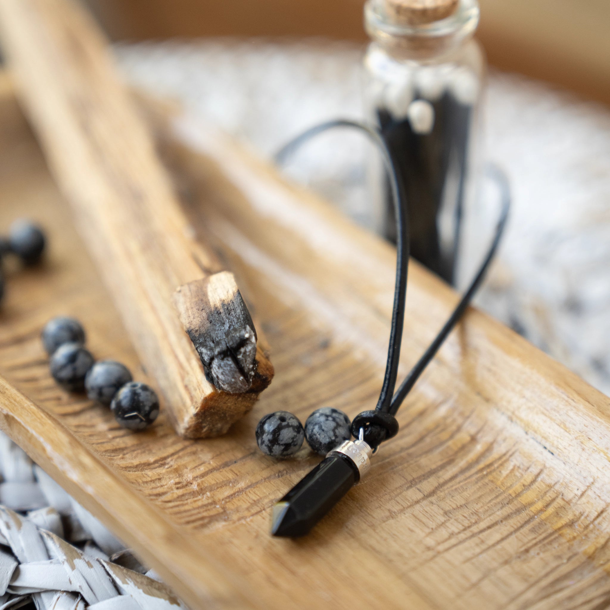 Obsidian protection pendant resting on wood beside black beads and charred wood