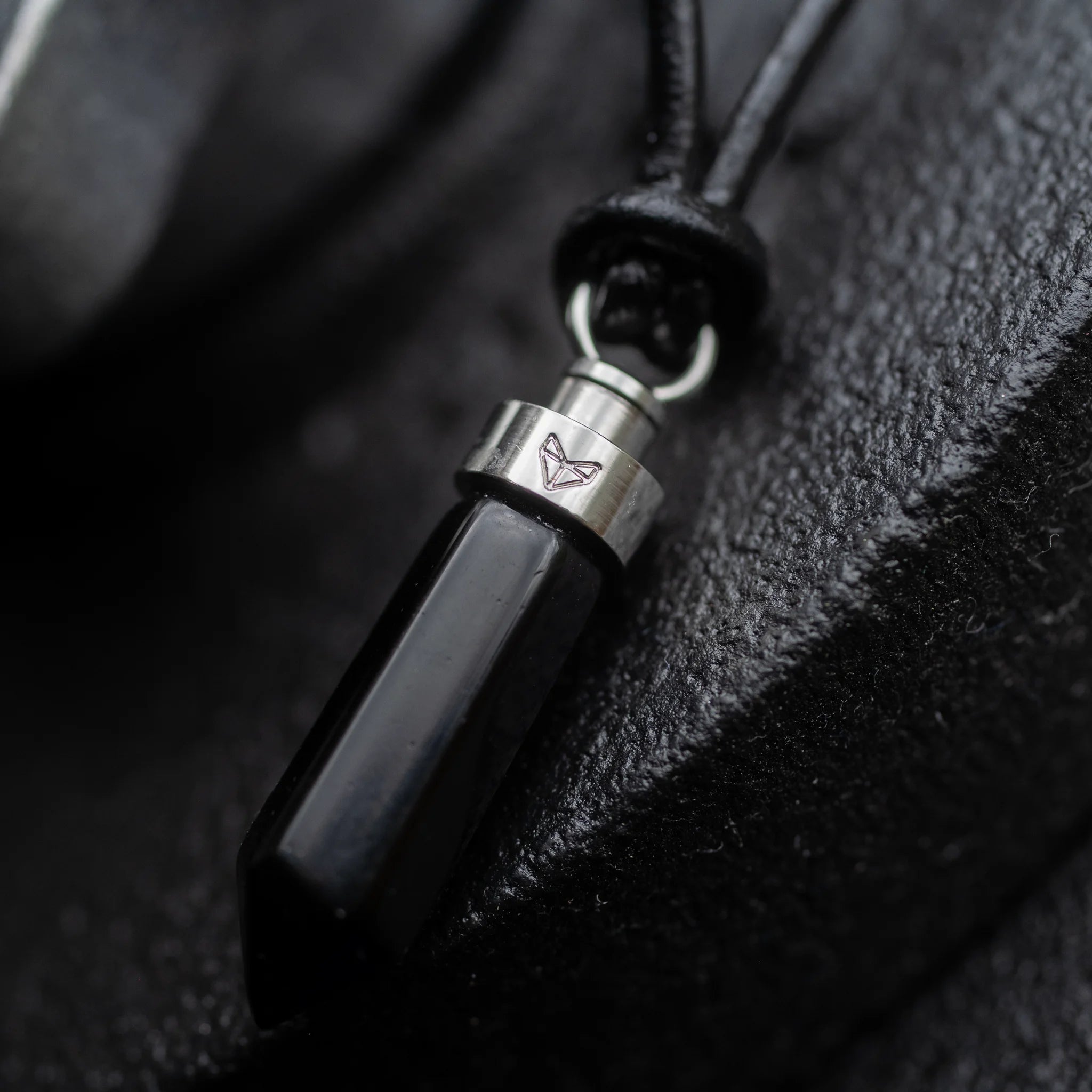 Close-up of obsidian protection pendant against rough black stone