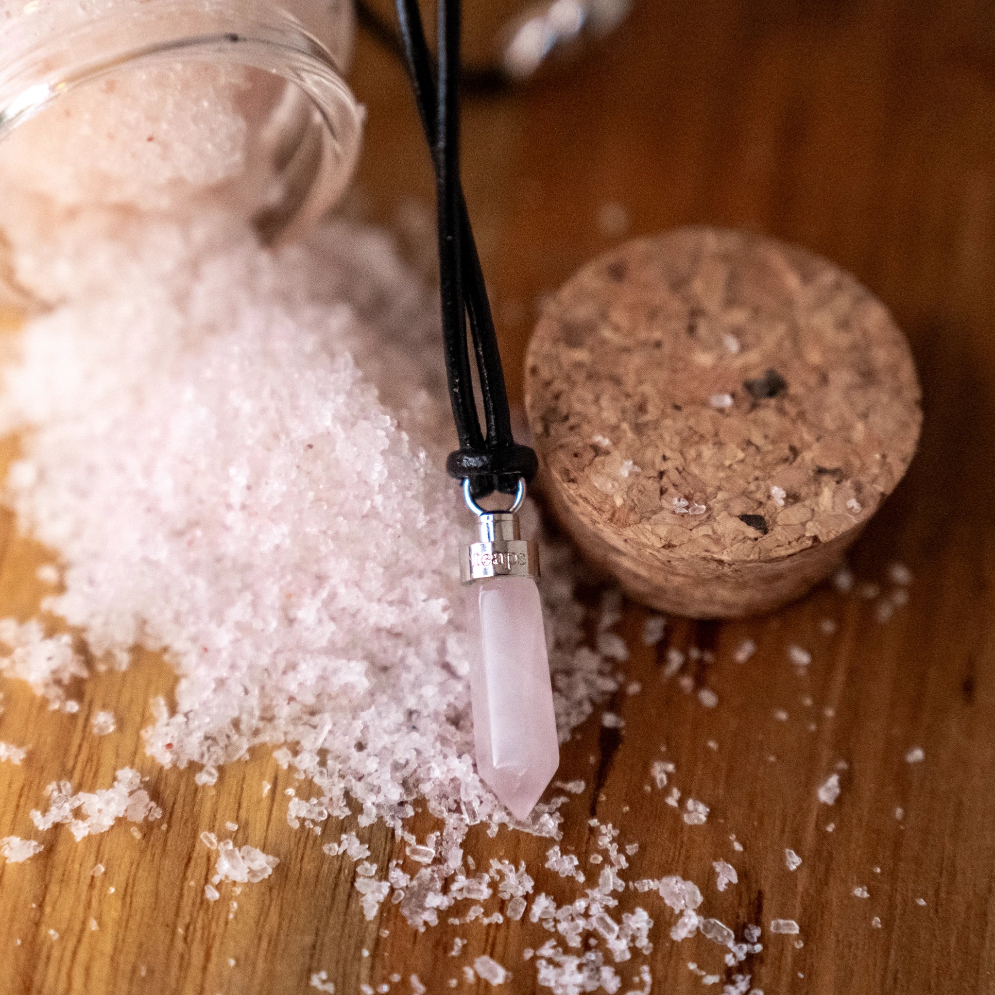 Rose quartz love pendant beside pink bath salts and cork jar